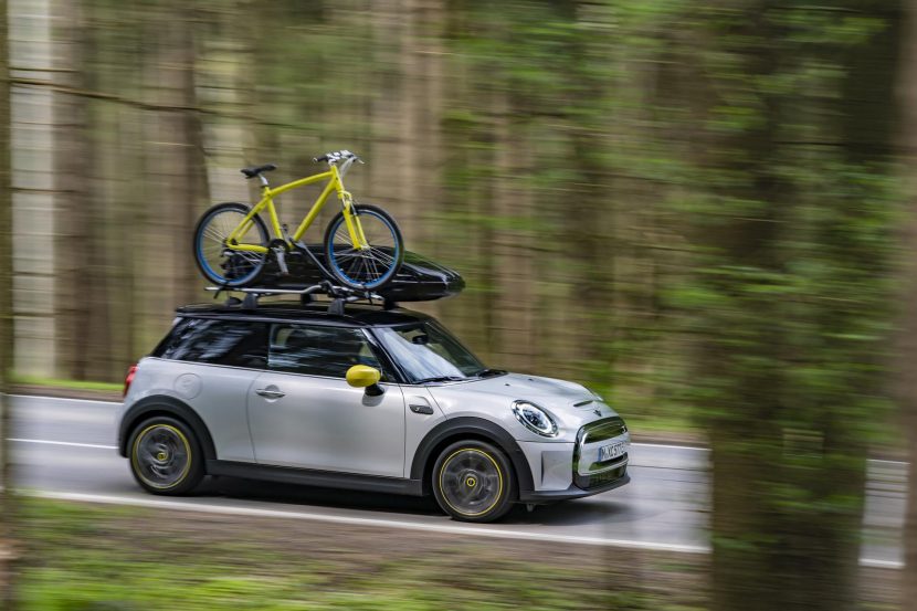Electric MINI Cooper SE driving on a backroad with a bike on top.